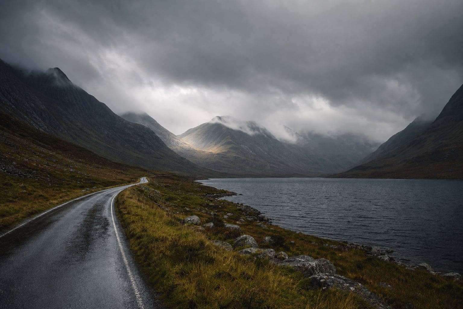 Winding wet road beside a dark Highland loch under low cloud