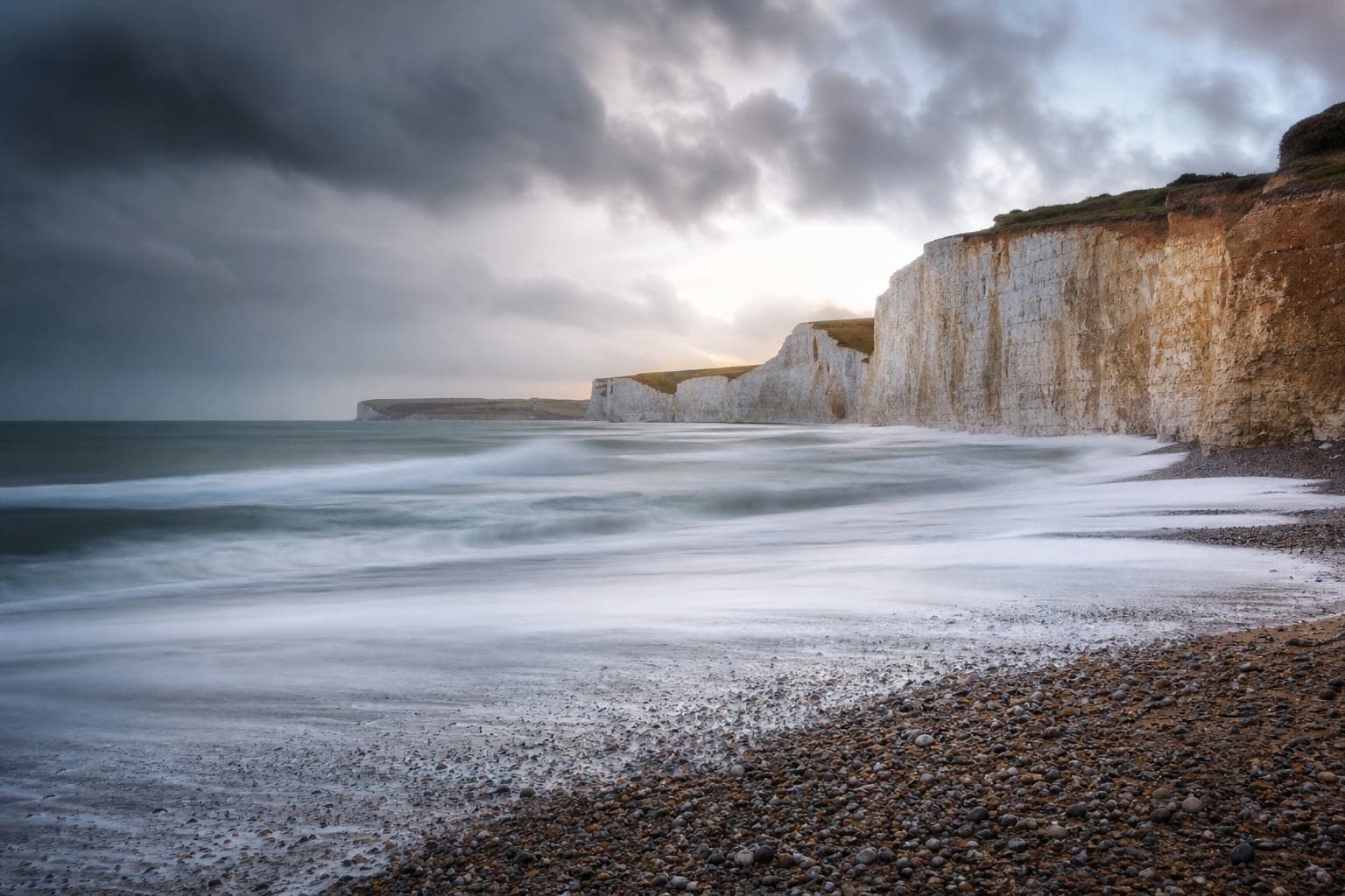 Chalk cliffs and a pebble beach beneath a clearing storm